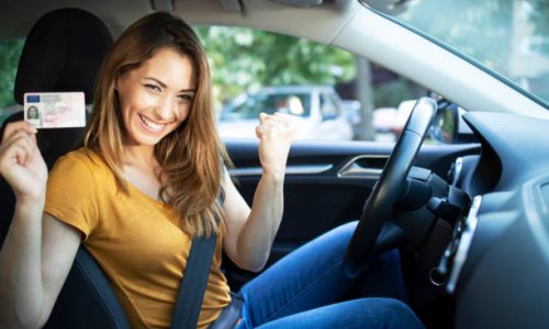 Car interior view of woman with driving license. Driving school. Young beautiful woman successfully passed driving school test. Female smiling and holding driver's license.